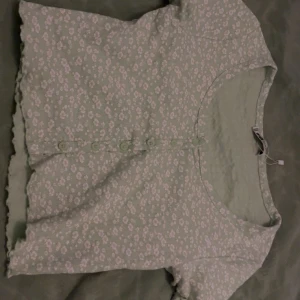 Grön blommig topp  - Söt grön topp med blommigt mönster från FB Sister. Toppen har korta ärmar och knappar framtill. 