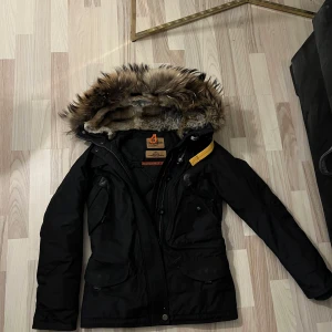 Parajumpers Doris jacka - Strl Xs. Svart Parajumpers Doris med avtagbara pälsdetaljer. Köpt på Johnells 2016 (året innan dom började använda certilogo). Sparsamt använd i 2-3 år. Jackan är varm, hel och fin men behöver tvättas då den legat i ett förråd resterande tiden ☺️Kostade 9995kr som ny!