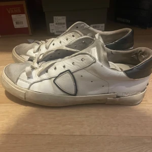 Vita sneakers från Philippe Model - Snygga vita sneakers från Philippe Model med svarta detaljer och snörning. Skorna har en klassisk design med en skön passform och är perfekta för en avslappnad stil.                                   -Trasig sula på båda skorna                                           -Lacar dom vid ev köp