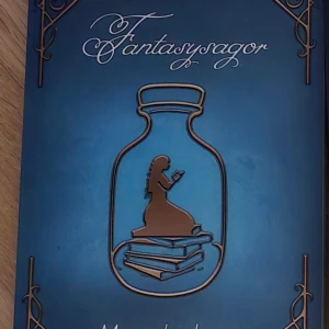 Fantasysagor - En vackert designad bok med titeln 'Fantasysagor'. Omslaget är i en djup blå färg med dekorativa hörn och en silhuett av en flicka som sitter på en hög med böcker inuti en flaska. Perfekt för fantasyälskare som vill försvinna in i magiska berättelser.
