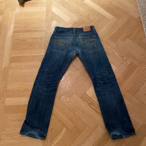 Vintage jeans från Nudie Jeans - Säljer ett par snygga vintage jeans från Nudie Jeans med klassisk femficksdesign och orange sömmar. Jeansen har en straight passform och är tillverkade i slitstarkt denim. Modellen är Average Joe i färgen dry sleveage som slutades säljas för ett bra tag sedan. 