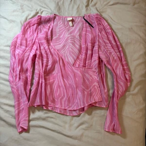 Rosa omlottblus från H&M - Säljer en rosa omlottblus från H&M med ett zebramönster. Blusen har långa ärmar och en djup v-ringning. Perfekt för en trendig look!