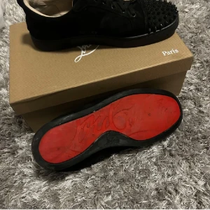 Svarta sneakers med nitar från Christian Louboutin - Snygga svarta sneakers från Christian Louboutin med ikoniska röda sulor. Skorna har nitar på tån och snörning framtill. Perfekta för att ge en edgy touch till din stil.