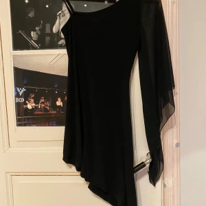 Svart oneshoulder klänning - Elegant svart oneshoulder klänning med asymmetrisk design och transparenta detaljer. Perfekt för en stilfull kväll.