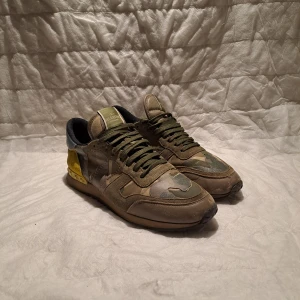 Valentino Rockrunner - Ett par äkta och Snygga Valentino  ny pris rumt 6000kr. Rockrunner sneakers i ett coolt camouflage-mönster. Skorna har gröna snören och en unik design med inslag av gult och blått. Perfekta för dig som vill sticka ut med stil. Storlek 43men passar även 44. Skorna är bra skick bara att två nitar har lossnat, det är inte jätte tydligt så märks nästan inte. Bara fråga om en bild i dm så löser jag. Box o dustbag medkommer inte. Pris kan diskuteras! Hör av er vid fler frågor!