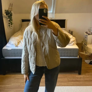 Beige/Kakhi quiltad jacka från H&M - Säljer en beige quiltad jacka från H&M. Jackan har en normal passform med långa ärmar och knappar framtill. Perfekt för höst och vår.