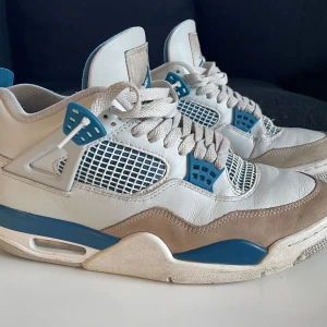 Nike Air Jordan sneakers i vitt och blått - Säljer ett par klassiska Nike Air Jordan sneakers i vitt och blått. Skorna har snörning och en ikonisk design med blå detaljer och Nike Air-logga på hälen.