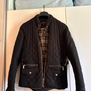 Svart quiltad jacka från Hollies - Snygg svart quiltad jacka från Hollies med dragkedja och knappar.  Perfekt för höst och vår. Jackan har inga slitage. 