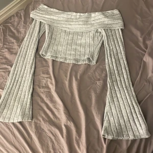 Grå ribbad offshoulder topp från Shein - Säljer en snygg grå ribbad offshoulder topp från Shein. Toppen har långa ärmar och en croppad passform, perfekt för en trendig look. Passar utmärkt till både jeans och kjol.