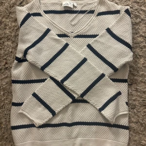 Vit och marinblå randig tröja från Isolde - Säljer en stilren vit tröja från Isolde med marinblå ränder och v-ringning. Tröjan har en texturerad yta och långa ärmar, perfekt för en avslappnad look.