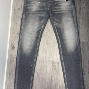 Grå Dsquared2 jeans - Snygga grå jeans från Dsquared2 med en unik blekt effekt och stänkdetaljer. De har en klassisk femficksdesign och en röd etikett med logotypen baktill. Perfekta för en trendig look. Pris kan diskuteras vid snabb affär!!
