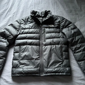 Svart dunjacka från The North Face - Säljer en svart dunjacka från The North Face med broderad logga och 550-dunfyllning. Jackan har en dragkedja framtill och långa ärmar. Perfekt för kyliga dagar. Använd i en säsong och i bra skick.