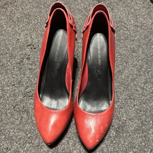 Röda pumps från Redherring Milano - Snygga röda pumps med spetsig tå och klack från Redherring Milano. Perfekta för att ge en färgklick till din outfit. De har en elegant design med en liten remdetalj vid hälen. Den går mest mot rosa isch svårt med ljuset. 