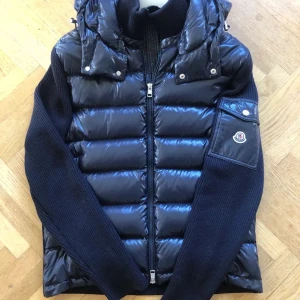 Mörkblå cardigan från Moncler - Snygg mörkblå cardigan från Moncler med quiltad design och huva. Jackan har långa ärmar och en dragkedja framtill. Perfekt för kyligare dagar.