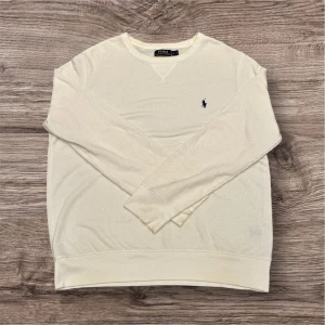 Ralph Lauren tröja - Säljer en stilren vit tröja från Ralph Lauren! Har en pytte liten fläck på armen den syns knapp i normalt ljus. Tröjan kan ha tappat lite färg men är fortfarande i mycket bra skick! Den är även lite nopprig! 