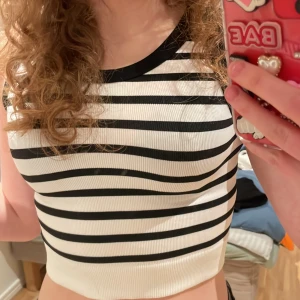 Randig ärmlös topp - Säljer en stilren svartvit randig topp med ärmlös design. Perfekt för en avslappnad look. Toppen är croppad och har en ribbad kant. Köpt i därav osäker på märke, pris kan sänkas!!