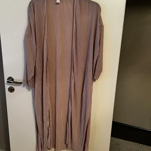 Beige lång kimono från H&M - Säljer en elegant beige lång kimono från H&M. Den har ett randigt mönster och är tillverkad i ett lätt och luftigt material. Perfekt för att lägga till en stilfull touch till din outfit.