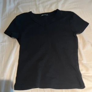 Svart v-ringad t-shirt från Zara - Snygg svart v-ringad t-shirt från Zara i mjukt material. Perfekt basplagg för alla tillfällen. Kortärmad design som passar bra till både jeans och kjol.