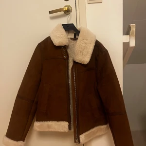Brun mockajacka med foder - Snygg brun mockajacka med mjukt vitt foder och dragkedja. Jackan har en klassisk krage och långa ärmar. Perfekt för kyligare dagar🩷