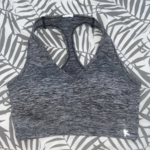 Grå sporttopp med brottarrygg - Snygg och bekväm grå sporttopp med brottarrygg. Perfekt för träning med sin stretchiga passform och mjuka material. Toppen har en diskret melerad design och en liten logga i nederkant. Står ej storlek men gissar på s/m. Mycket bra skick!