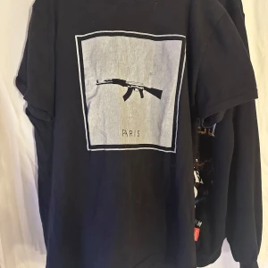 Svart t-shirt från Defend Paris - Snygg svart t-shirt från Defend Paris med ett tryck av ett gevär och texten 'Paris'   Säljs då jag inte använder den mer och den har blivit lite förstörd på märket men annars skön att ha på sig 