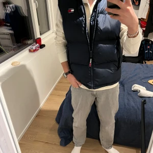 Svart dunväst från Tommy Hilfiger - Snygg svart dunväst från Tommy Hilfiger med dragkedja och broderad logga på bröstet. Perfekt för lager-på-lager under kyliga dagar. Västen har en klassisk design och är lätt att matcha med olika outfits.