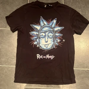 Svart Rick and Morty t-shirt - Säljer en svart t-shirt med ett coolt Rick and Morty-tryck på framsidan. Perfekt för fans av serien! T-shirten är kortärmad och har en normal passform.