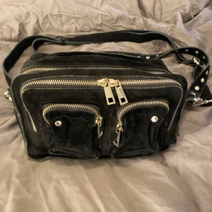 Svart väska ifrån Nunoo  - Säljer nu min svarta Nunoo väska, osäker på vad den är i för storlek men skulle gissa på medium. Den kommer med ett kortare axelband och ett avtagbart samt justerbart crossbodyband. 