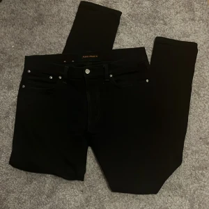 Svarta jeans från Nudie Jeans - Snygga svarta jeans från Nudie Jeans i ekologisk bomull. De har en klassisk design med dragkedja och knappar. Perfekta för en stilren look.