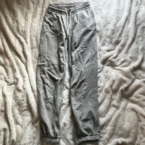 Grå mjukisbyxor från H&M - Säljer ett par grå mjukisbyxor från H&M Basics. Byxorna har en elastisk midja med snörning och muddar vid bensluten för en bekväm passform. Perfekta för en avslappnad stil. Mått syns på sista bilderna, har också sytt om de till mer lågmidjade🤗