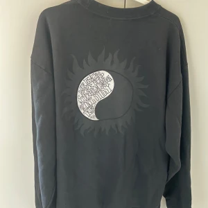 Our legacy x stussy work shop sweatshirt - Snygg svart sweatshirt från Stussy med ett unikt tryck på framsidan. Tröjan har långa ärmar och en rund halsringning. Perfekt för en avslappnad stil.