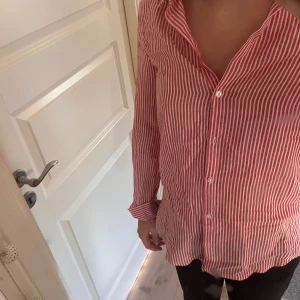 Röd och vit randig skjorta - Säljer en snygg röd och vit randig skjorta med långa ärmar. Skjortan har en klassisk krage och knappar hela vägen ner. Perfekt för både vardag och fest! 🥳