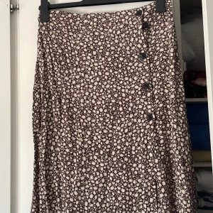 Midikjol från H&M - En brun blommig midi kjol från H&M.  Storlek 42. I mycket gott skick.  Kjolen har en slits på ena sidan. 