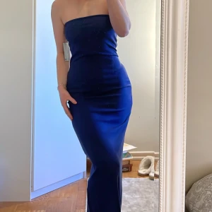 Klänning  - Säljer en oanvänd bandeau-klänning från NA-KD med lappen kvar, storlek M! Sitter supersnyggt och har även en slits där bak. Skriv vid mer info/bilder!