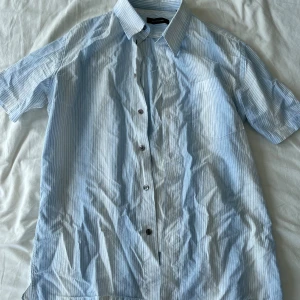 Ljusblå randig skjorta från Paul & friends - Säljer en cool ljusblå surfarskjorta från Paul & friends. Skjortan är kortärmad, randig och har knappar längs framsidan. Perfekt för sommarens alla tillfällen! Den är i bomull och väldigt bekväm att ha på sig. Skjortan är i bra skick och redo för en ny ägare. Frågor? Skriv!