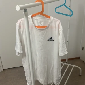 Vit t-shirt från Adidas - Säljer en klassisk vit t-shirt från Adidas i storlek S. Den har en enkel design med Adidas-loggan tryckt på bröstet. Perfekt för träning eller vardagsbruk. T-shirten är i bomull och har korta ärmar.
