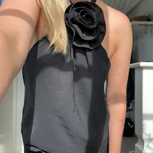 Svart topp med en blomma - Säljer min underbara topp från design by si som jag har använt en gång! Älskar den men den kommer tyvärr aldrig till användning! Den är öppen i ryggen och väldigt stretchig men en fin liten blomma framtill! Nypris: 271kr🖤