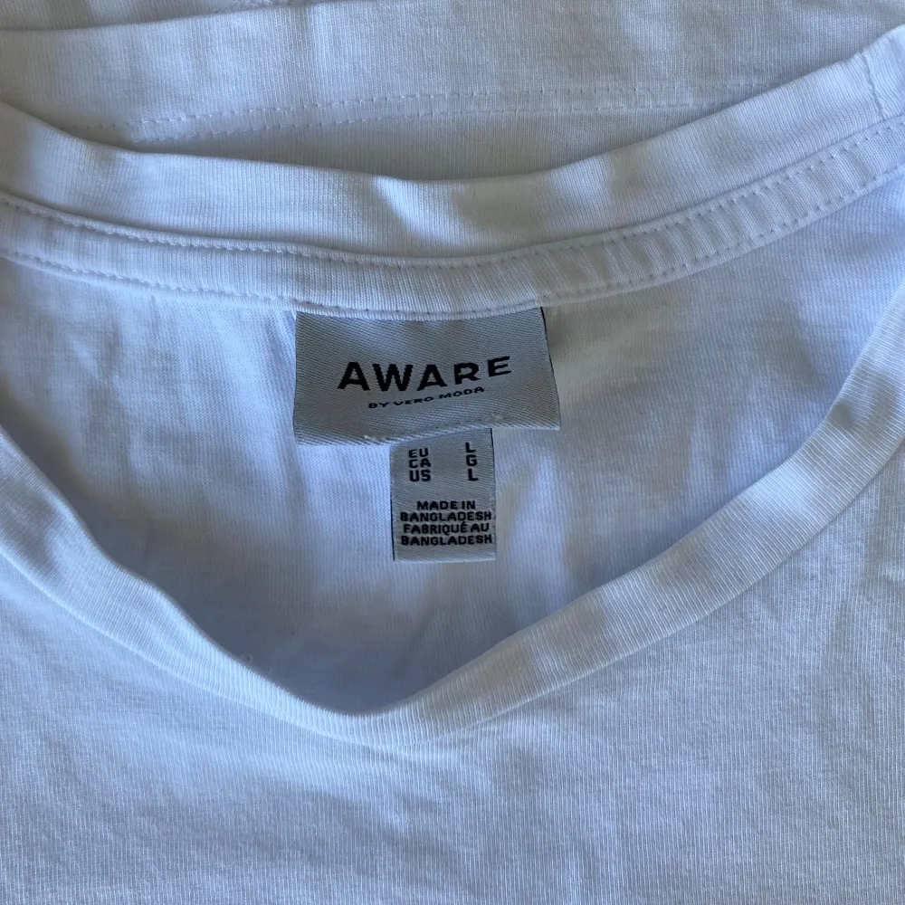 Säljer en klassisk vit t-shirt från Aware i storlek L. Den är gjord av mjuk bomull och har en normal passform med korta ärmar. Perfekt basplagg för alla tillfällen 💘. T-shirts.