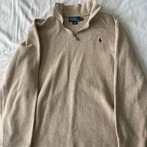 Beige tröja från Polo Ralph Lauren - Enligt mig en av Ralph Laurens snyggaste plagg. Grisch half-zip från Polo Ralph Lauren i storlek M. Den är gjord av 100% bomull och har en premium dragkedja framtill. Perfekt för höst och vår med sin stilrena design och bekväma passform. Tröjan har långa ärmar och en liten broderad logga på bröstet. Passar både till vardags och lite finare tillfällen! Frågor? Skriv!