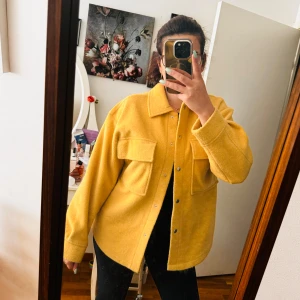 Gul overshirt från Gina Tricot - Säljer en superfin gul overshirt från Gina Tricot i storlek XS passar även som S/M .Den har en härlig, varm gul färg och är perfekt för höst och vår. Jackan har långa ärmar och knappar framtill. Den är i nyskick och har två stora fickor på bröstet. Perfekt för att lägga till lite färg i din garderob!