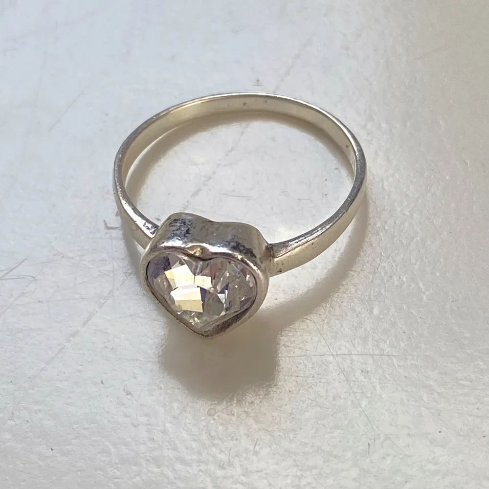 Säljer en vacker silverring med en stor, glittrande hjärtformad sten. Ringen är i bra skick och har en elegant och tidlös design. Perfekt för speciella tillfällen eller som en fin present. Märkt med 'Sasb' och är inte magnetisk så jag tror det är silver . Accessoarer.