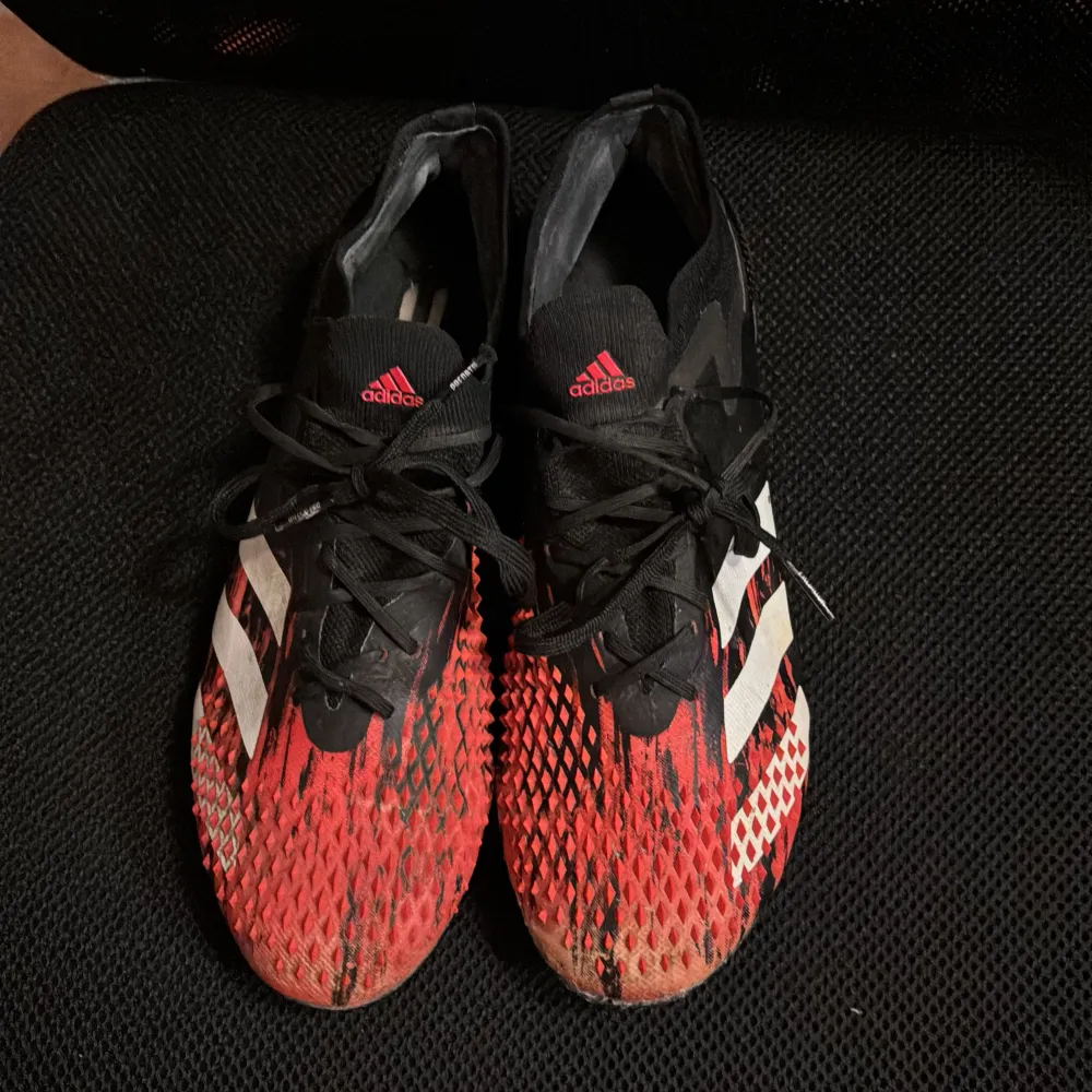 täljer ett par Adidas Predator fotbollsskor i svart och röd färg. Skorna har en cool design med snörning och är perfekta för fotbollsträning eller match. De har en tight passform och är i bra skick.skicket är 7,2/10.org pris 1100. Skor.