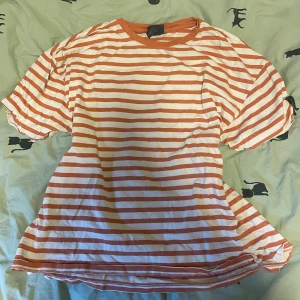 Randig t-shirt i orange och vit - Säljer en superfin randig t-shirt i orange och vit. Perfekt till hösten. Materialet känns mjukt och skönt mot huden. Passar både till jeans och shorts för en avslappnad look!