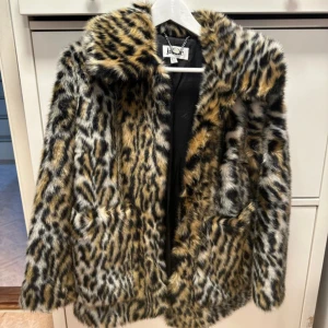 Leopardmönstrad pälsjacka från Jakke - Säljer en supercool leopardmönstrad pälsjacka från Jakke. Den är perfekt för att sticka ut i mängden och hålla sig varm samtidigt. Jackan har en klassisk krage och är långärmad. Den är i nyskick och har en snygg kedjedetalj vid nacken. Perfekt för höst och vinter!