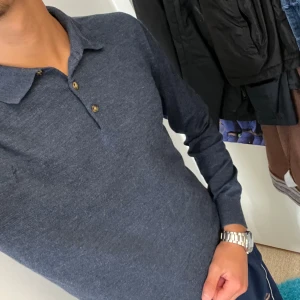 Mörkblå pikétröja från John Henric - Säljer en stilren mörkblå pikétröja från John Henric. Tröjan har långa ärmar och tre knappar vid kragen. Perfekt för både vardag och lite finare tillfällen. Den är i bra skick men har några små märken på axeln, vilket syns på bilderna. Passar perfekt till höst- och vårgarderoben!