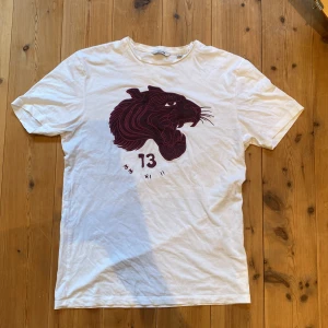 Vit t-shirt med pantermotiv från Only & Sons - Säljer en cool vit t-shirt från Only & Sons med ett stort pantermotiv i vinrött på framsidan. T-shirten är i bomull och har en normal passform. Perfekt för en avslappnad stil!