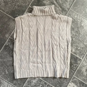 Beige stickad väst med polokrage - Säljer en supermysig grå stickad väst med polokrage. Perfekt för lager-på-lager under höst och vinter. Den har ett snyggt stickat mönster och är i ett mjukt material som känns skönt mot huden. Passar perfekt till både jeans och kjol! Storlek S men passar även M.
