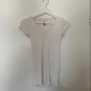 Vit T-shirt från Tally Weijl - Säljer en enkel och stilren vit T-shirt från Tally Weijl. Den har en v-ringad hals och korta ärmar, perfekt för vardagsbruk. Materialet känns mjukt och bekvämt, och det finns en liten broderad kanin längst ner som en söt detalj. Passar bra till både jeans och kjol!