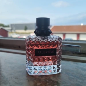 Valentino Donna Born in Roma Parfym - Säljer en lyxig Valentino Donna Born in Roma parfym. Flaskan är superfin med ett mönster av små nitar och en elegant svart kork. Parfymen har en härlig rosa färg som syns genom den genomskinliga glasflaskan. Perfekt för den som vill ha en doft som känns både modern och klassisk. Kommer i en snygg rosa kartong.