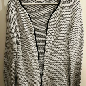 Svartvit mönstrad kofta från Only - Säljer en snygg svartvit mönstrad kofta från Only i storlek XL. Koftan har ett coolt geometriskt mönster och är perfekt för både vardag och fest. Den är långärmad och har en öppen design utan knappar eller dragkedja. Perfekt för vår och höst!
